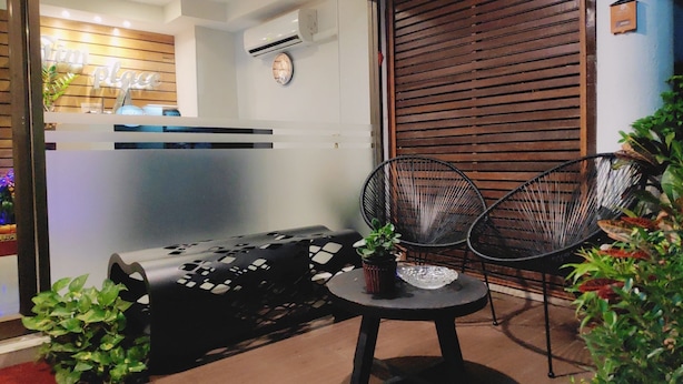 A modern reception area with a glass partition, a wooden slatted wall, and a seating area with two black chairs and a small table.