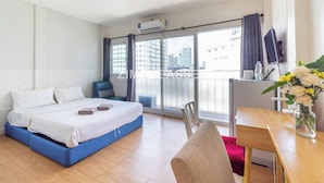 A modern hotel room with a large bed, a desk, and a view of the city through the balcony.