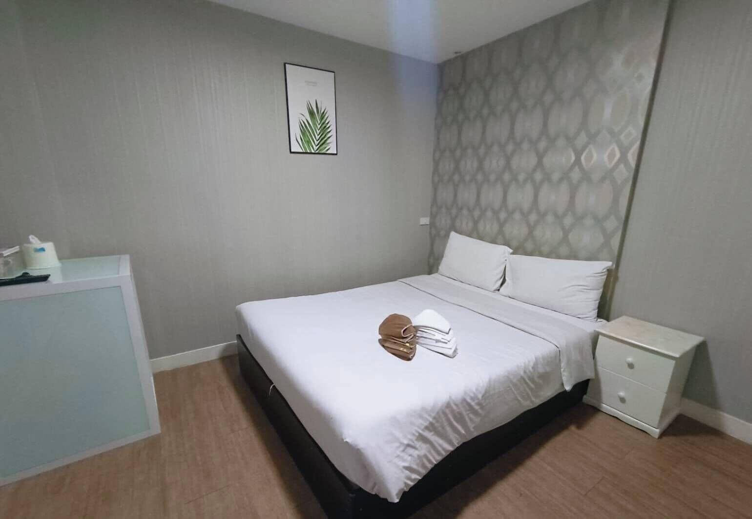 A neatly arranged hotel room with a bed, a bedside table, a desk, and a wall-mounted picture.