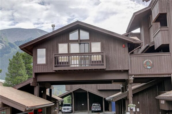 Un bâtiment en bois à deux étages, doté d’un balcon, d’un garage et surplombant un paysage montagneux.