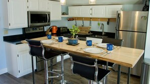 A modern kitchen with white cabinets, stainless steel appliances, and a wooden dining table with bar stools. - The Beach Haus on Copper Mountain Preview listing (Frisco)