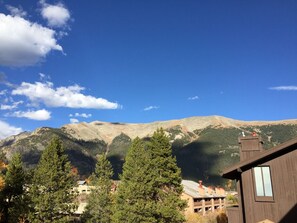 Un paysage de montagne avec un ciel dégagé, un bâtiment en bois doté d’une cheminée, et un bâtiment avec un toit rouge au premier plan.