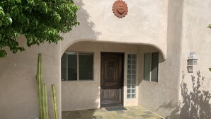 A building with a stucco exterior, a wooden door, and a tiled entrance area. - Tranquil Desert Retreat . Short walk to hot springs & close to Joshua Tree! (Desert Hot Springs)