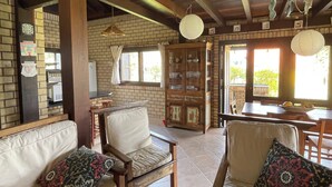 A cozy interior with a wooden ceiling, brick walls, and a tiled floor. There are two sofas with patterned cushions and a wooden cabinet with glass doors. - Beautiful house in Praia do Rosa overlooking the lagoon. (Praia do Rosa)