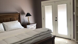 Ein Schlafzimmer mit einem großen Bett, einem Deckenventilator, einem Nachttisch mit Lampe und einer Tür mit Fenster.