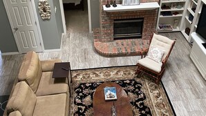 Ein Wohnzimmer mit Kamin aus Backstein, Deckenventilator, Sofa, Couchtisch und Bücherregal.