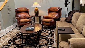 Ein Wohnzimmer mit großem Teppich, zwei Ledersesseln, einem Couchtisch und einem aufgehängten Hirschkopf an der Wand.