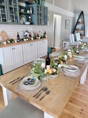 A long dining table set with plates, cutlery, and candles, surrounded by cabinets and a kitchen area. - Thanksgiving, Christmas, New Years available, room for family and friends🦃 ☃️🍾 (Elk Rapids)