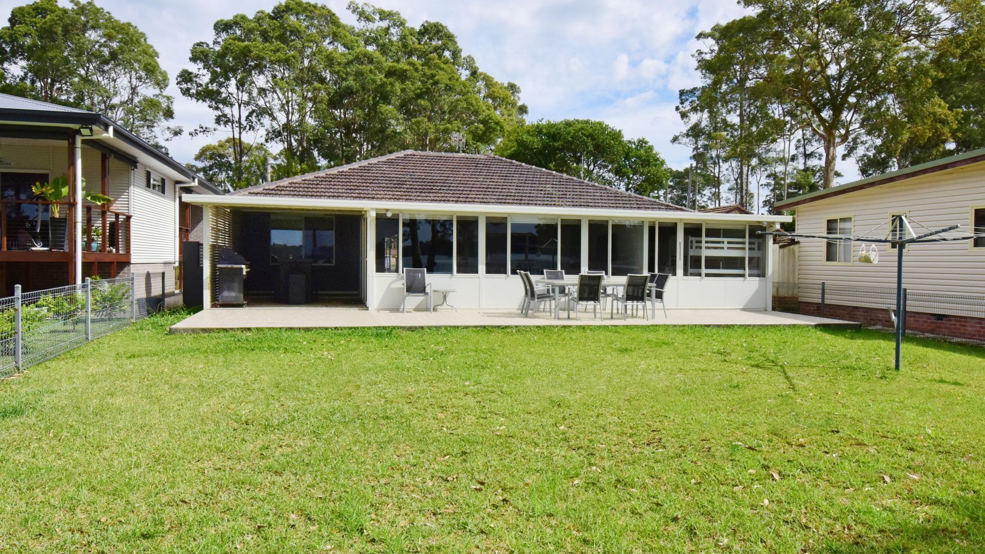 A house with a covered patio, a lawn, and trees in the background.