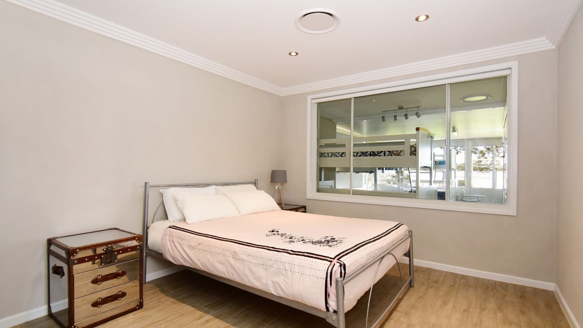 A bedroom with a bed, a nightstand, a dresser, and a large window.