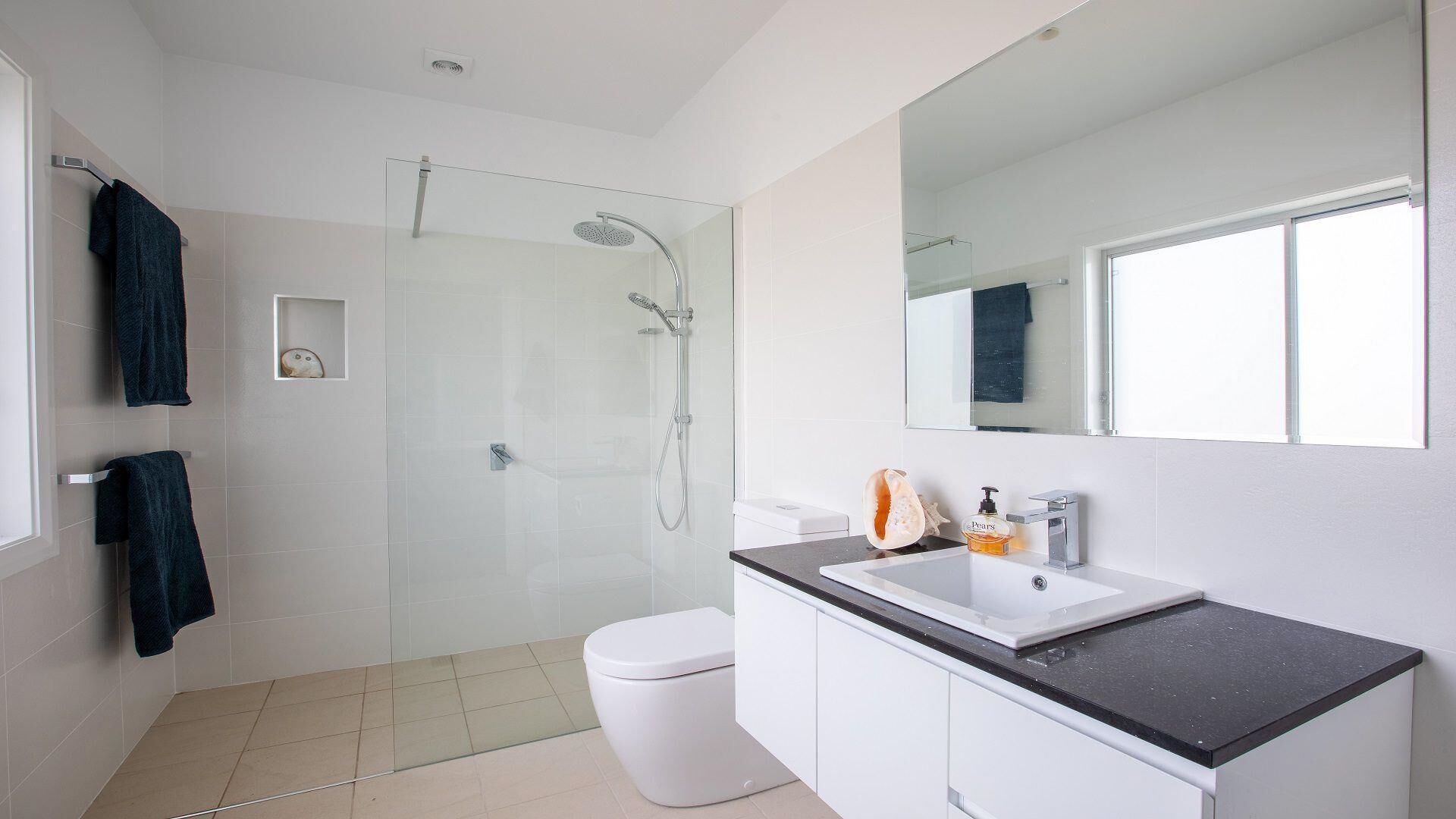 Een moderne badkamer met een douchecabine van glas, een wit toilet en een wastafelmeubel met een wastafel en spiegel.