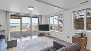 A spacious living room with a large TV, sliding glass doors to a balcony, and a view of the outdoors. - Lake Condo- Right on the Water with a Dock! Bring a boat or rent a boat! (Clear Lake)