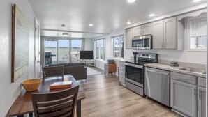 A modern kitchen with stainless steel appliances, a dining area with a wooden table and chairs, and a large window overlooking a scenic view. - Lake Condo- Right on the Water with a Dock! Bring a boat or rent a boat! (Clear Lake)