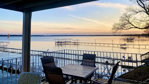 A covered outdoor seating area with a table and chairs, overlooking a calm body of water with docks and boats. - Lake Condo- Right on the Water with a Dock! Bring a boat or rent a boat! (Clear Lake)