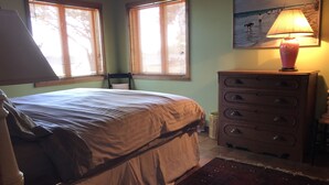 Un dormitorio con cama, cómoda, lámpara y un cuadro en la pared.