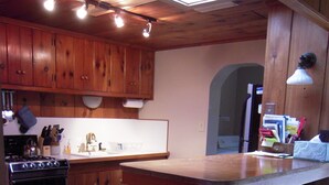 Cocina con armarios de madera, estufa, lavaplatos y taburetes de bar.