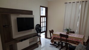 Una sala de estar con un televisor de pantalla plana, un mueble de madera para entretenimiento, una mesa de comedor con sillas y un sofá con un cojín estampado de leopardo.