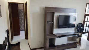 Una sala de estar con televisor montado en un mueble bajo de madera, un ventilador y un tapete estampado.