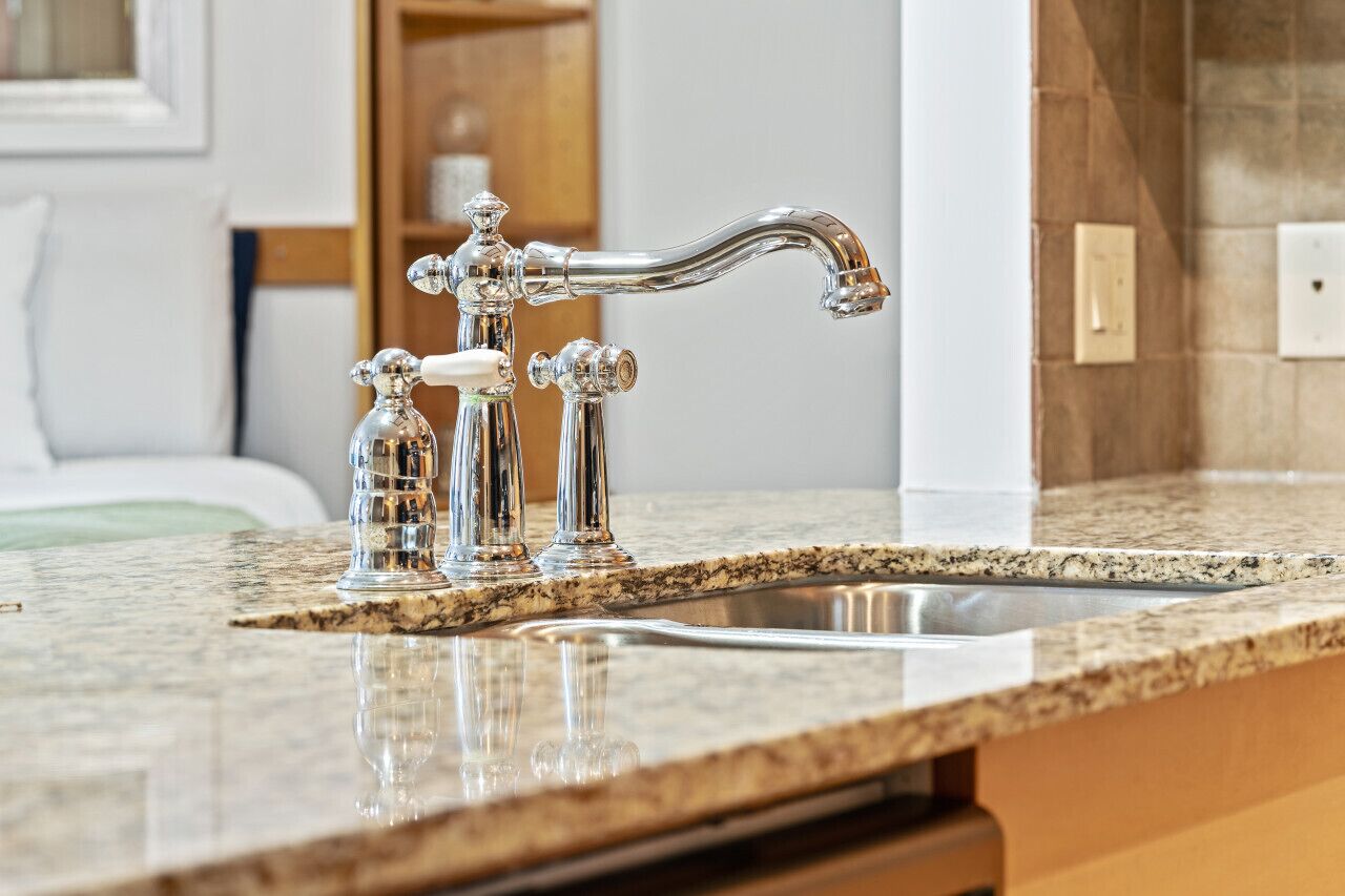 A kitchen with a granite countertop, stainless steel sink, and a silver faucet with multiple handles.