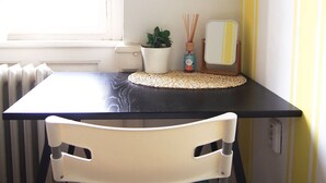 A dining table with a black top, a white chair with a floral pattern, a potted plant, and a framed artwork on the wall.