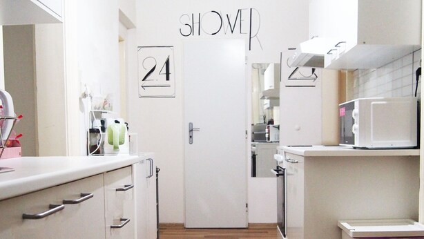 A modern kitchen with white cabinetry, a microwave, and a toaster. A door with the number 24 is visible, indicating room numbers.