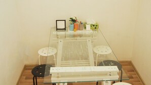 A glass-top dining table with four white stools, a small framed picture, and a decorative banner on the wall.