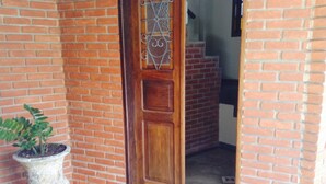 Eine Holztür mit dekorativem Metallgitter, ein Blumentopf und eine Treppe, die zu einer oberen Ebene führt.