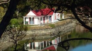 A small house with a red roof, surrounded by trees and a body of water.