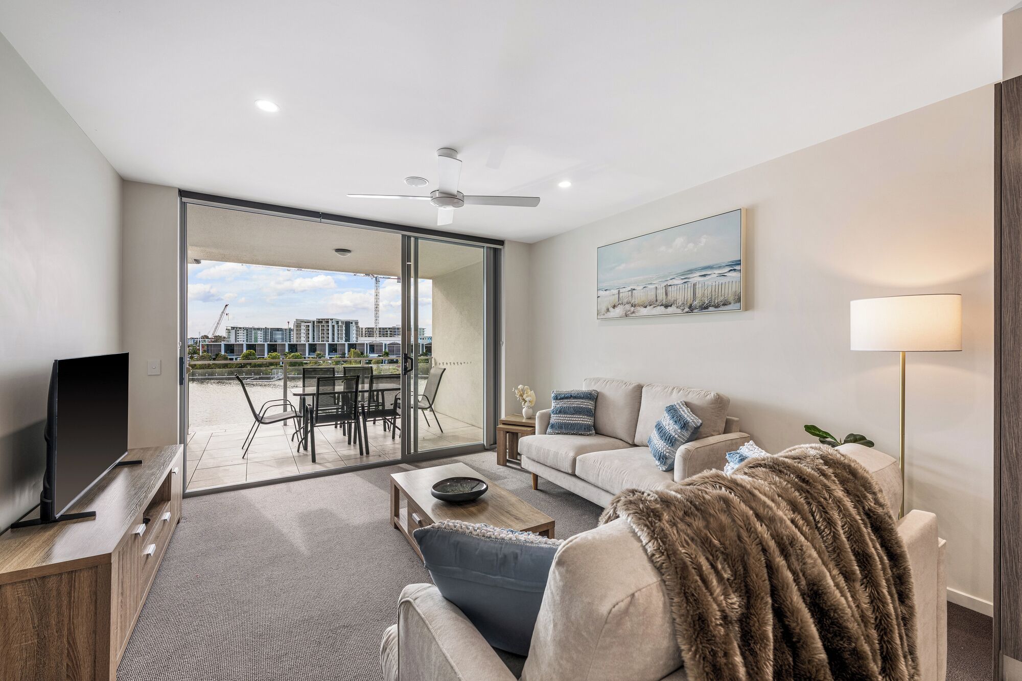 A modern living room with a flat-screen TV, a sofa, a coffee table, and a view of a balcony with outdoor furniture.