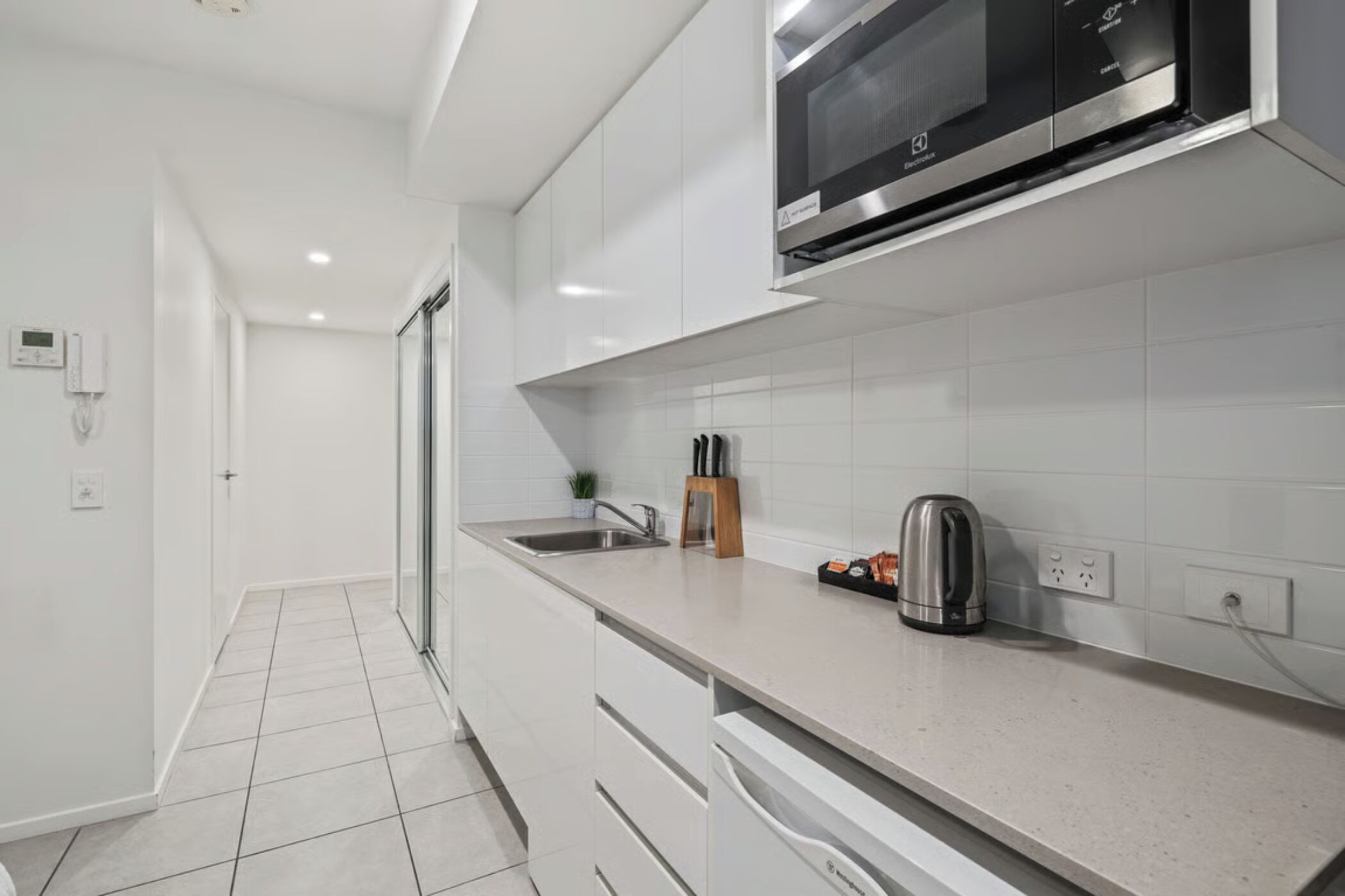 A modern kitchen with white cabinets, a stainless steel microwave, a kettle, and a knife block.