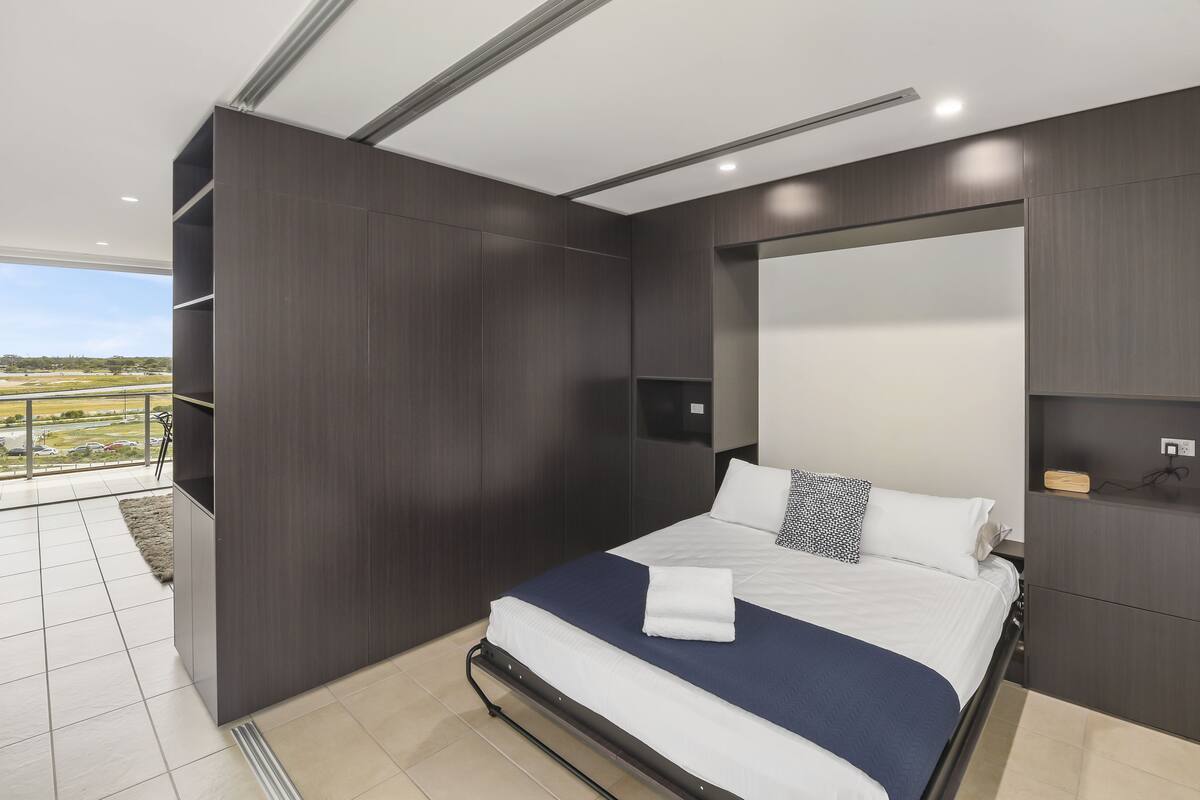 Een moderne slaapkamer met een groot bed, donker houten lambrisering, een ingebouwde televisie en uitzicht op de omgeving.