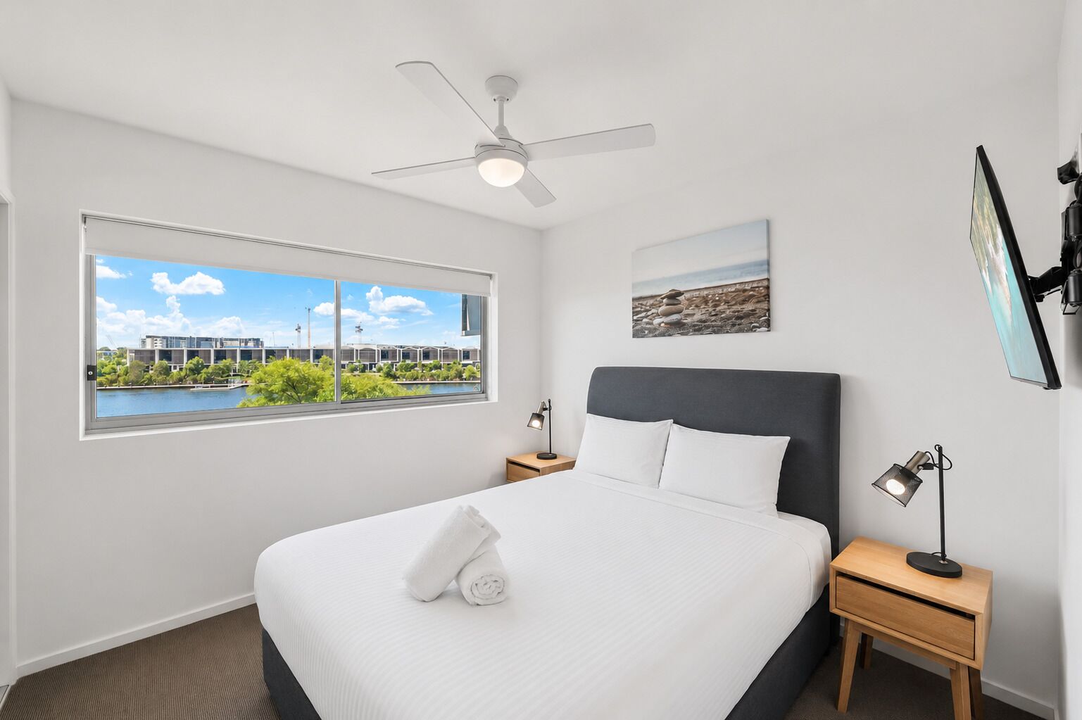 A hotel room with a bed, a ceiling fan, a window with a view, a bedside table, and a nightstand.