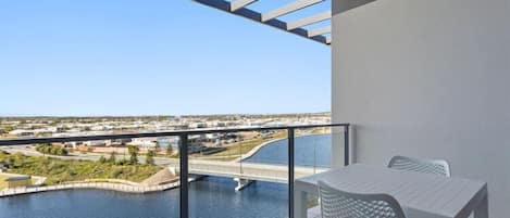 A balcony with a table and chairs overlooking a river and a bridge.