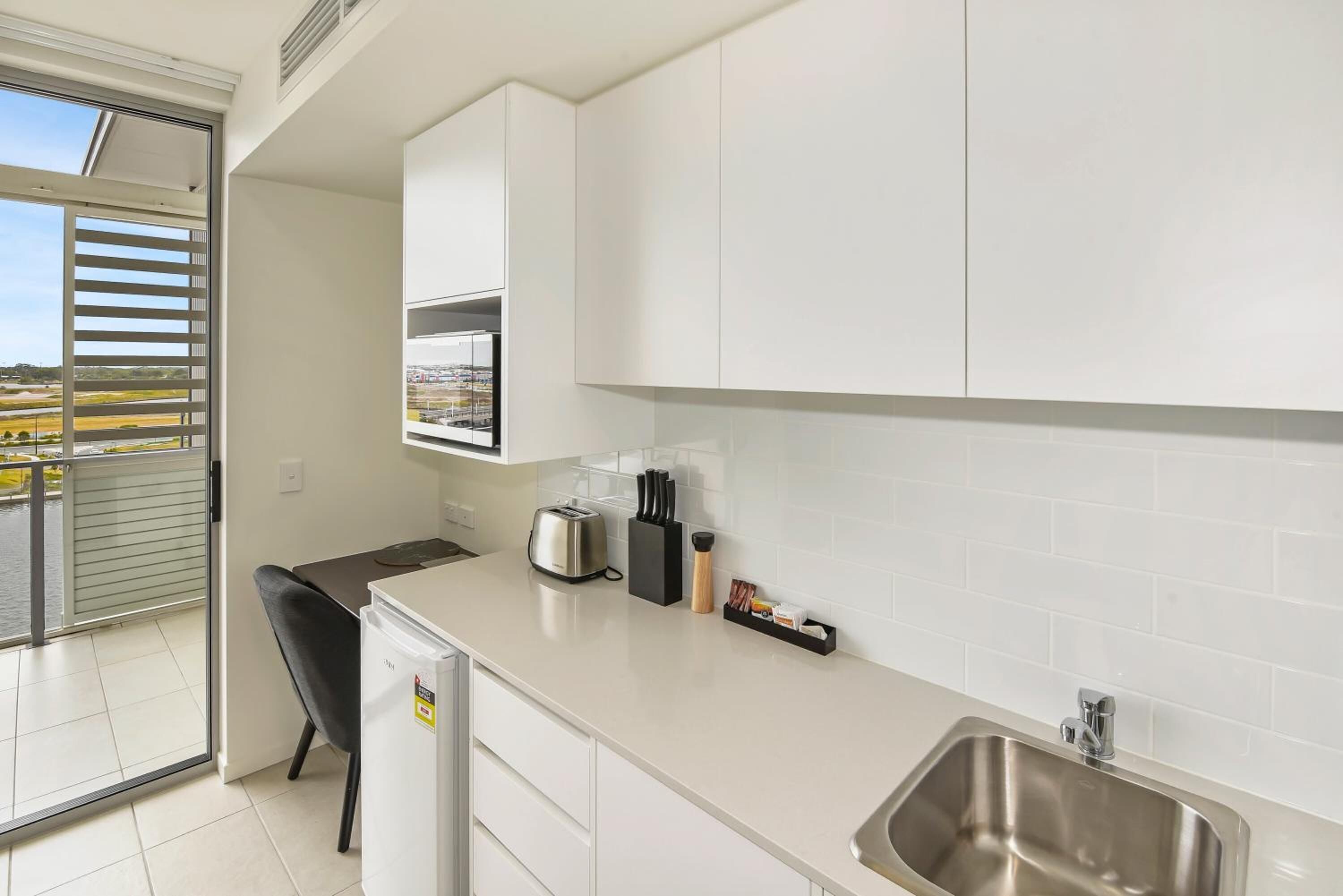 Una cocina moderna con armarios blancos, un lavamanos de acero inoxidable y un refrigerador pequeño.