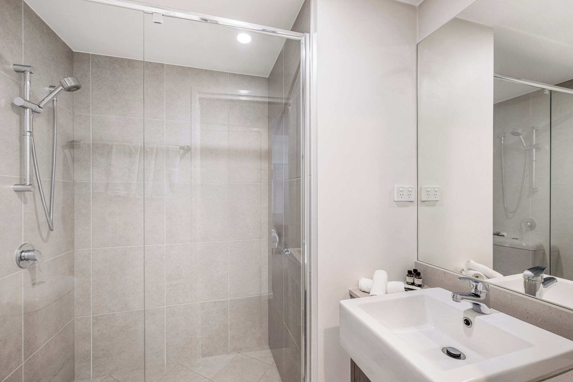 A modern bathroom with a glass-enclosed shower, a white sink, and a mirror.