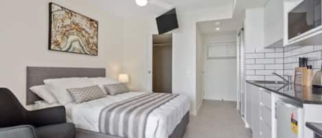 Una camera da letto con un letto, una sedia, una ventola a soffitto, una TV e un angolo cottura con un forno a microonde.