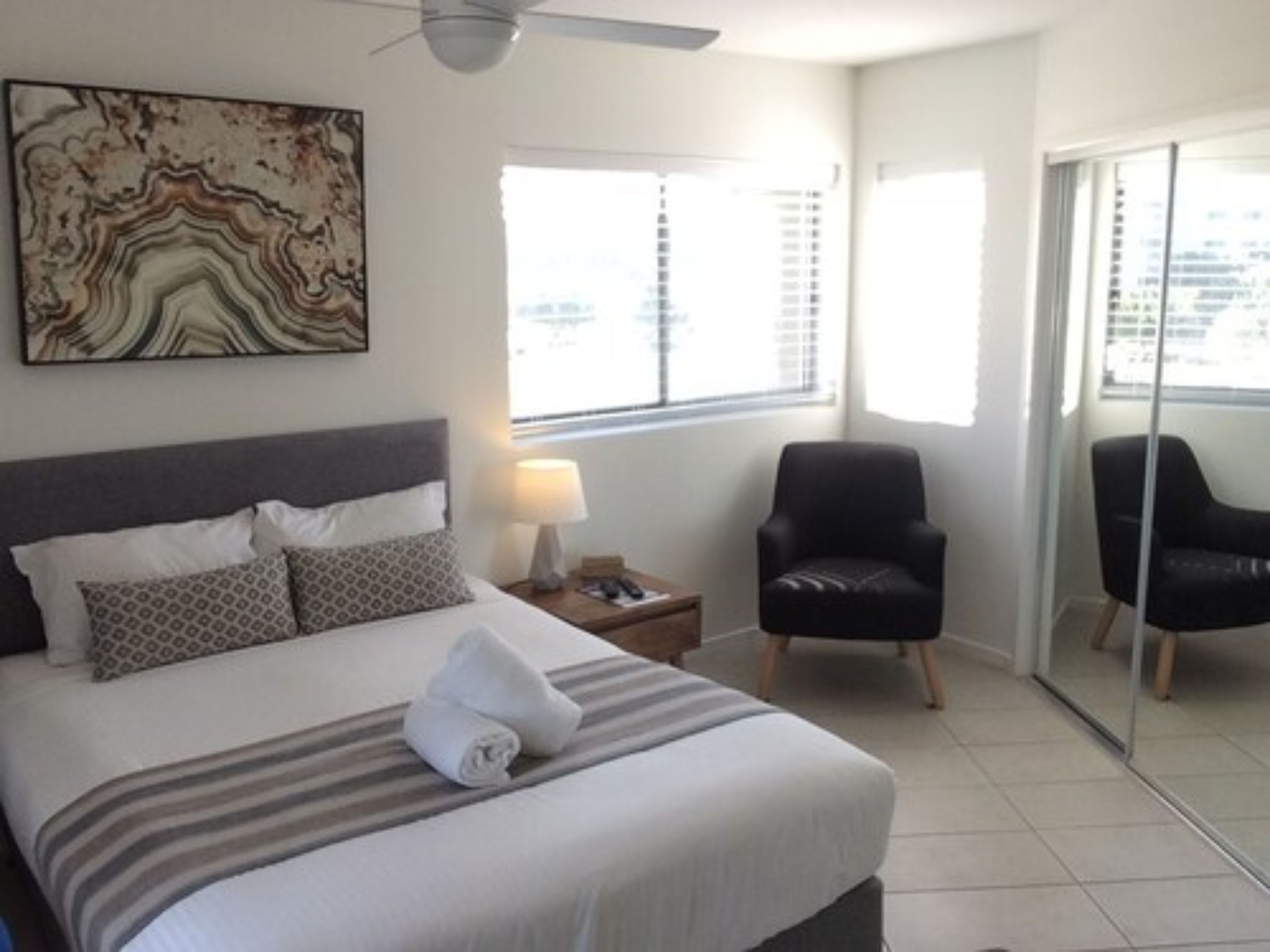 Una habitación de hotel con una cama, una silla, una lámpara y un ventanal grande.