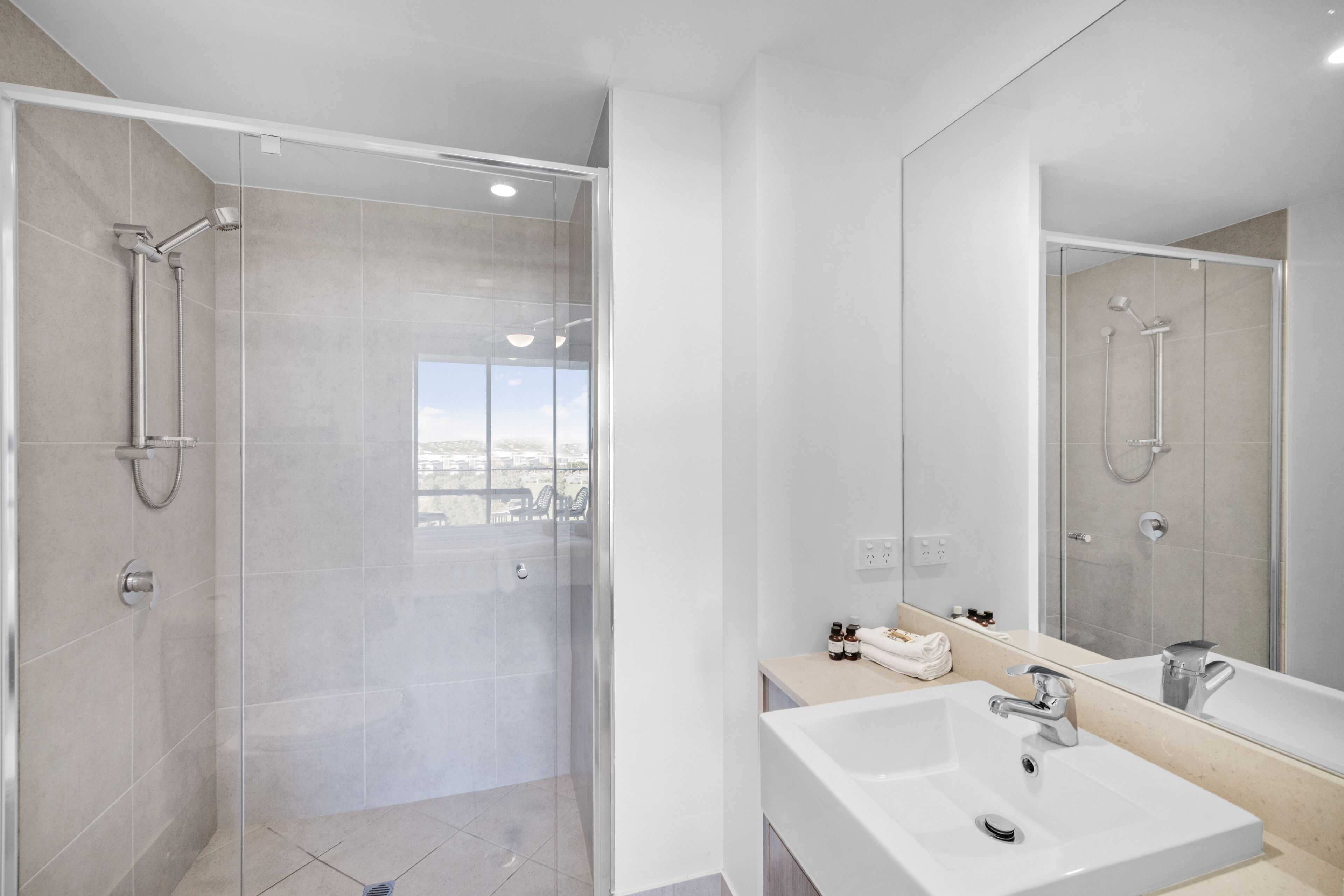A modern bathroom with a glass-enclosed shower, a large mirror, and a sink with a vanity.