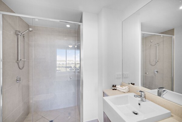 Een moderne badkamer met een douchecabine van glas, een grote spiegel en een wastafel met een badkamermeubel.