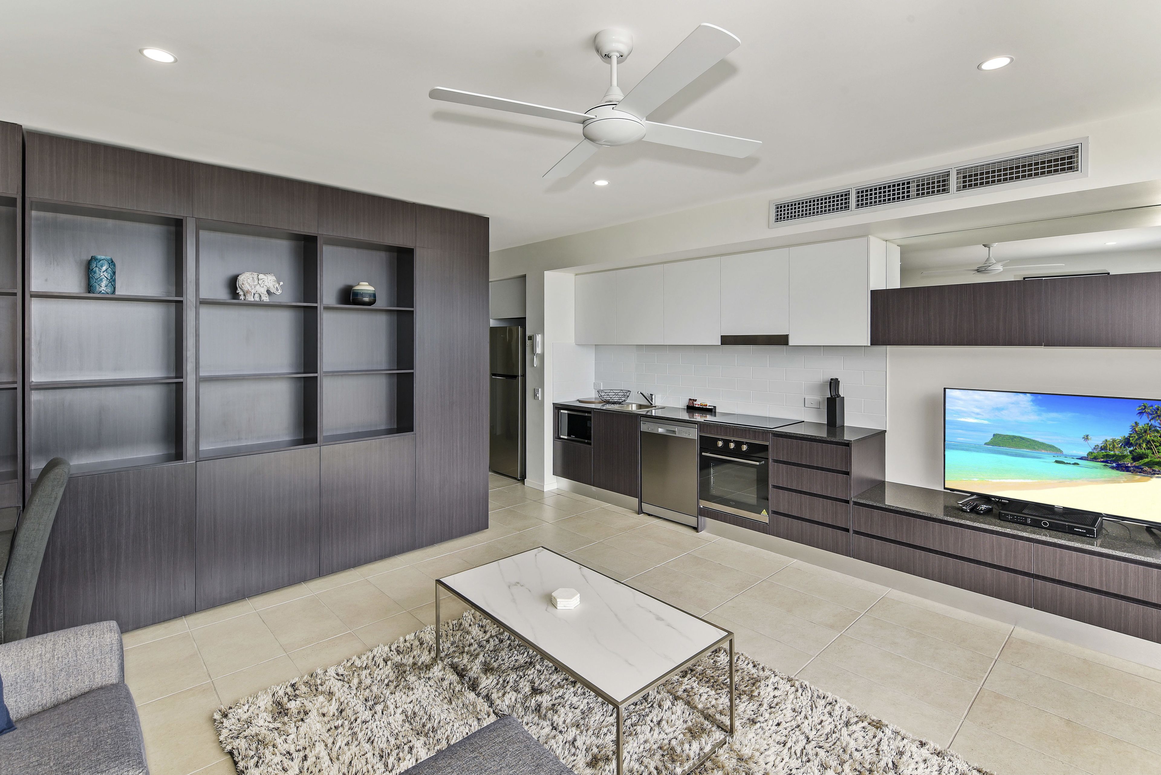 Una cocina moderna con horno integrado, un comedor con mesa de mármol y una sala de estar con sofá y ventilador de techo.