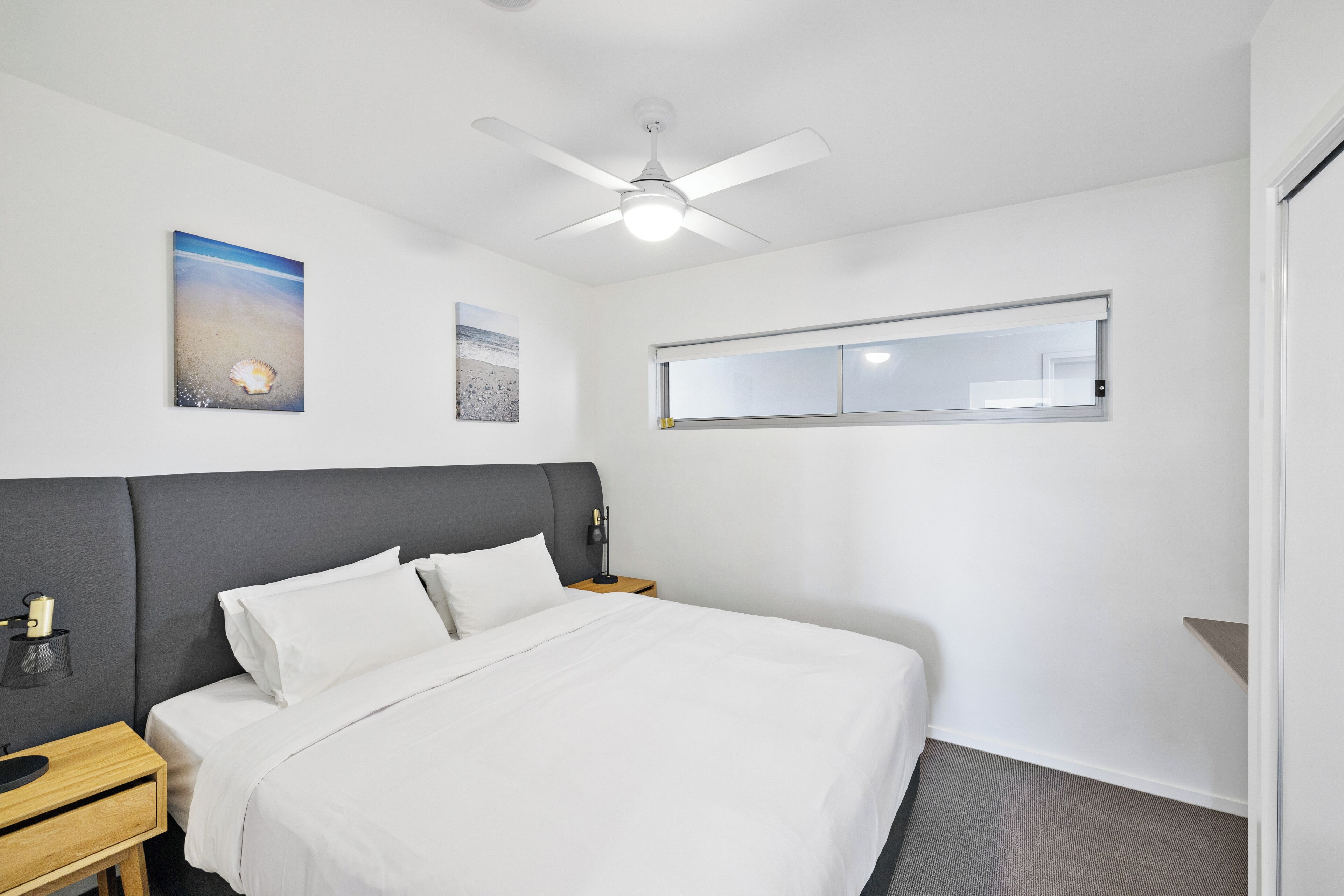 Ein Hotelzimmer mit Bett, Deckenventilator, Nachttisch und Fenster.