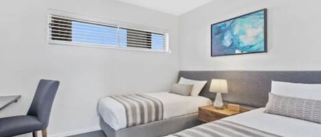 A hotel room with a bed, a chair, a nightstand, a lamp, a ceiling fan, and a window with blinds.