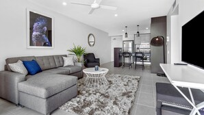 A modern living room with a grey sectional sofa, a round coffee table, and a flat-screen TV. - North Shore Kawana and Waterline (Birtinya)