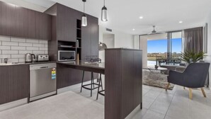 A modern kitchen with dark wood cabinets, a built-in oven, and a bar area with stools. - North Shore Kawana and Waterline (Birtinya)