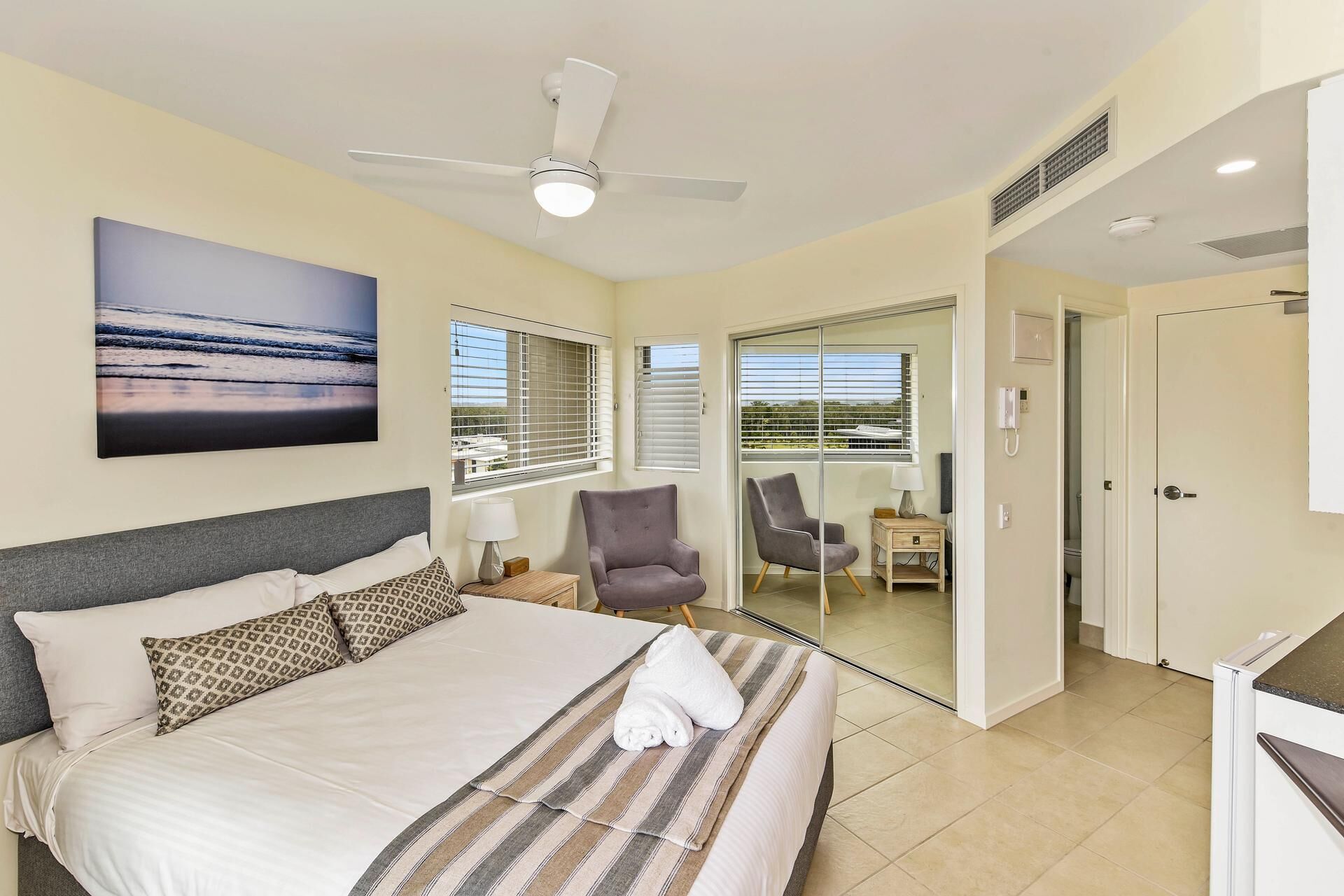 Habitación de hotel con cama, ventilador de techo, vistas al exterior, una silla y una mesita.
