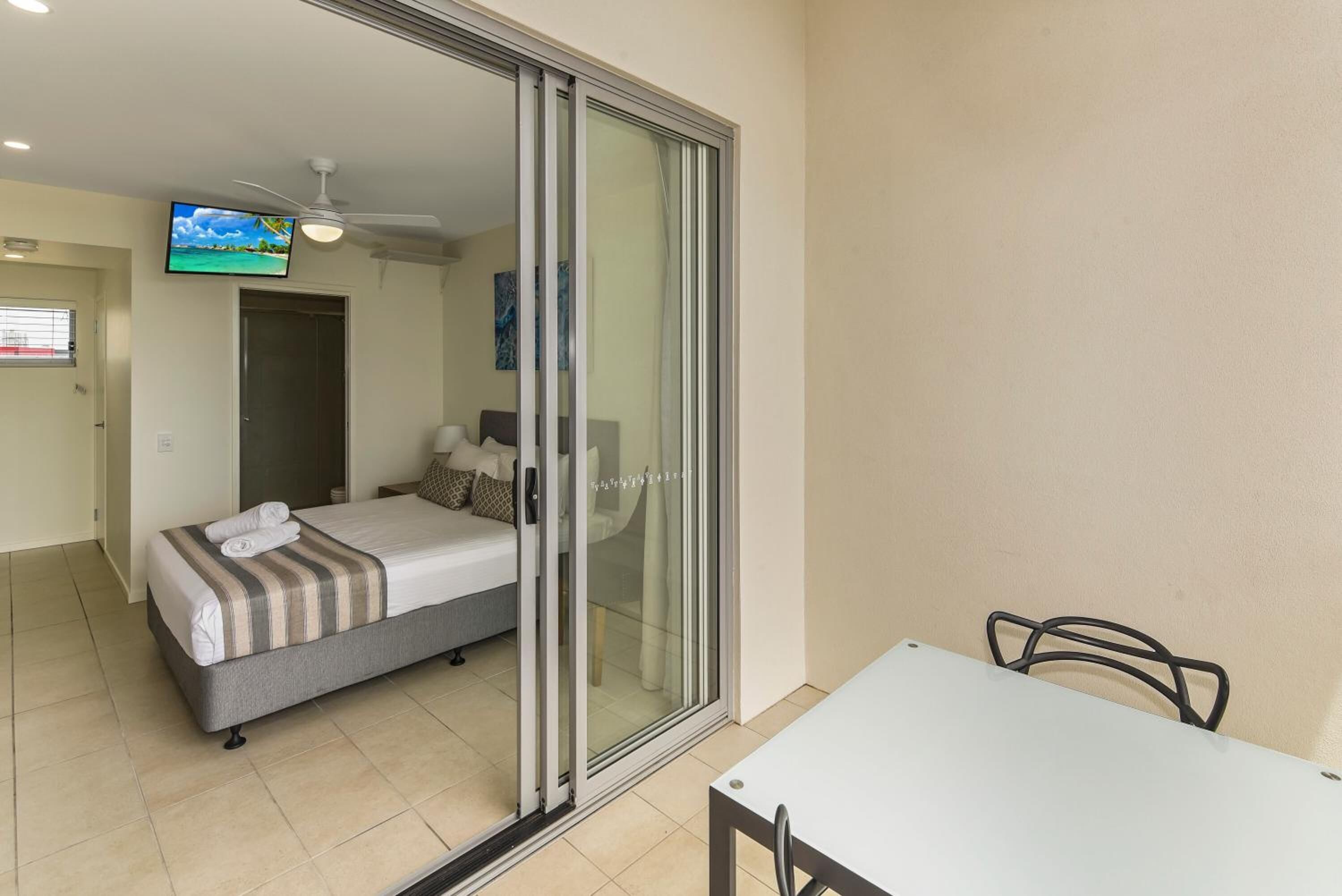 A bedroom with a bed, a sliding glass door, a ceiling fan, a TV, and a door leading to another room.