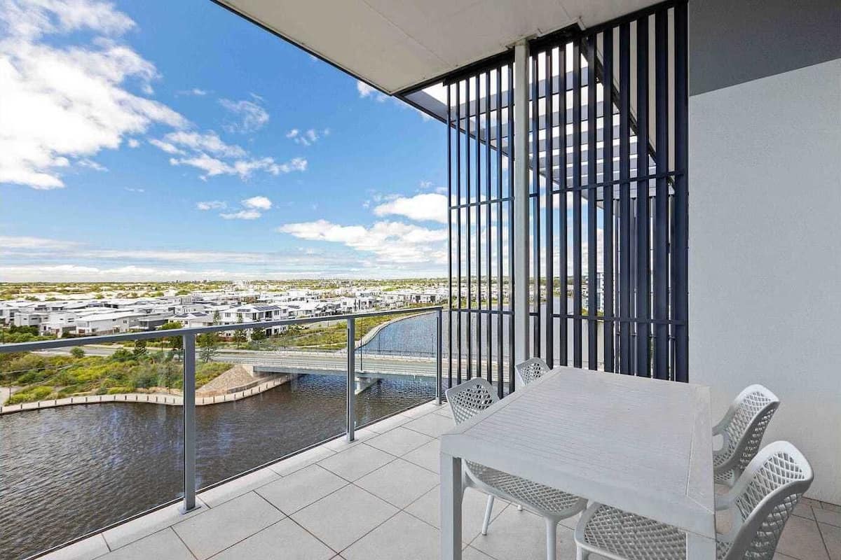 Een balkon met een tafel en stoelen, met uitzicht op een waterpartij en een brug.