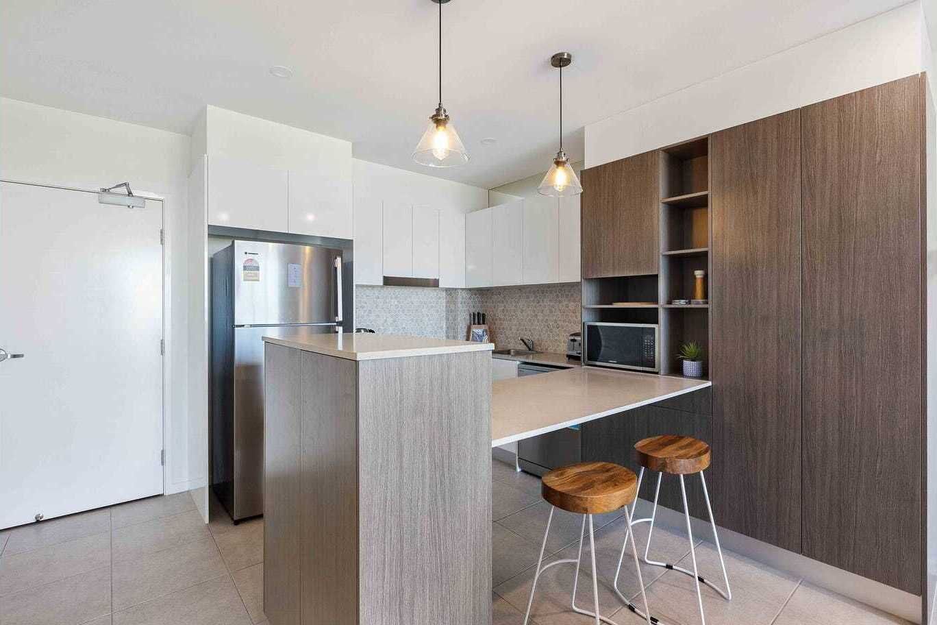Eine moderne Küche mit einer zentralen Kochinsel, Barhocker, einem Kühlschrank und Holzschränken.