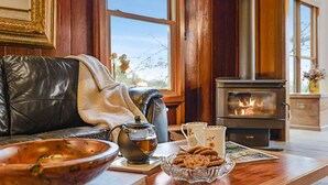 Un salón acogedor con un sofá de cuero, una mesa con tetera, galletas y un cuenco. Se ve una chimenea al fondo.