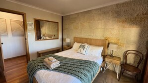 Un dormitorio con una cama de madera, una pared de piedra, un espejo, una mesita de noche con una lámpara y una silla.